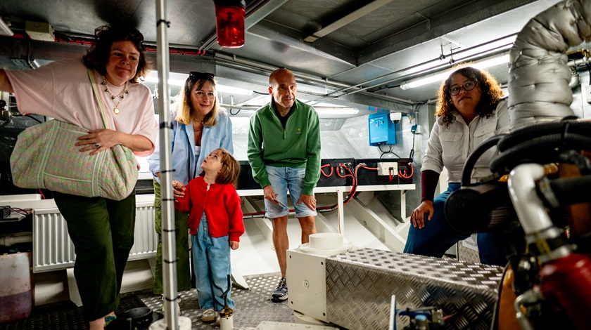 Des adultes et un enfant visitent la salle des machines d’un bateau avec une membre de l’équipage.